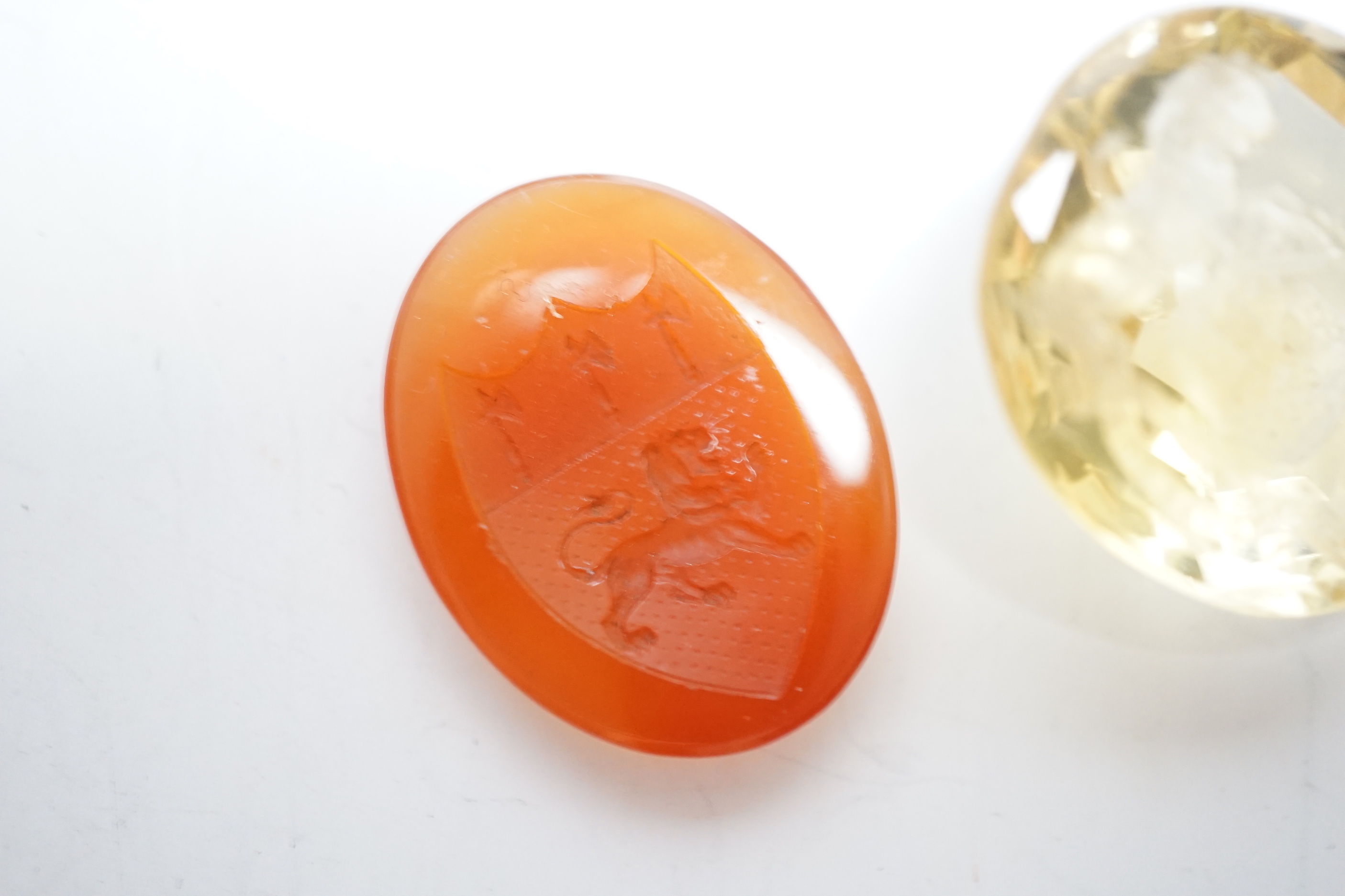 An unmounted oval cut intaglio citrine, 28mm by 25mm and a similar carnelian intaglio, both matrix carved with armorial/crest.